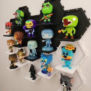 May include: A black hexagonal shelf unit with white shelves displays a collection of pop culture figurines, including characters from Star Wars, He-Man, Tom and Jerry, and Scooby Doo.