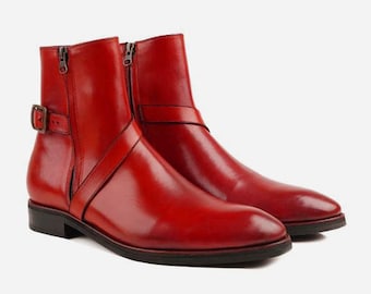 Pode incluir: Um par de botas de tornozelo de couro vermelho com uma fivela e fecho de correr.