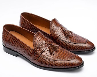 May include: A pair of brown leather loafers with a snakeskin pattern and tassel accents.