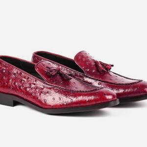 May include: A pair of red leather loafers with a tassel detail. The loafers have an ostrich print pattern.