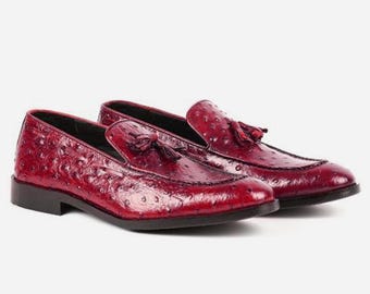 May include: A pair of red leather loafers with a tassel detail. The loafers have an ostrich print pattern.