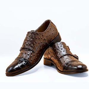 Könnte beinhalten: Ein Paar braune Lederschuhe mit Schnallenverschluss. Die Schuhe haben ein Straußenmuster und eine spitze Zehenpartie.