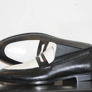 May include: A pair of black and white leather loafers. The loafers have a white leather toe and a black leather heel. The loafers are a classic style and would be perfect for any occasion.