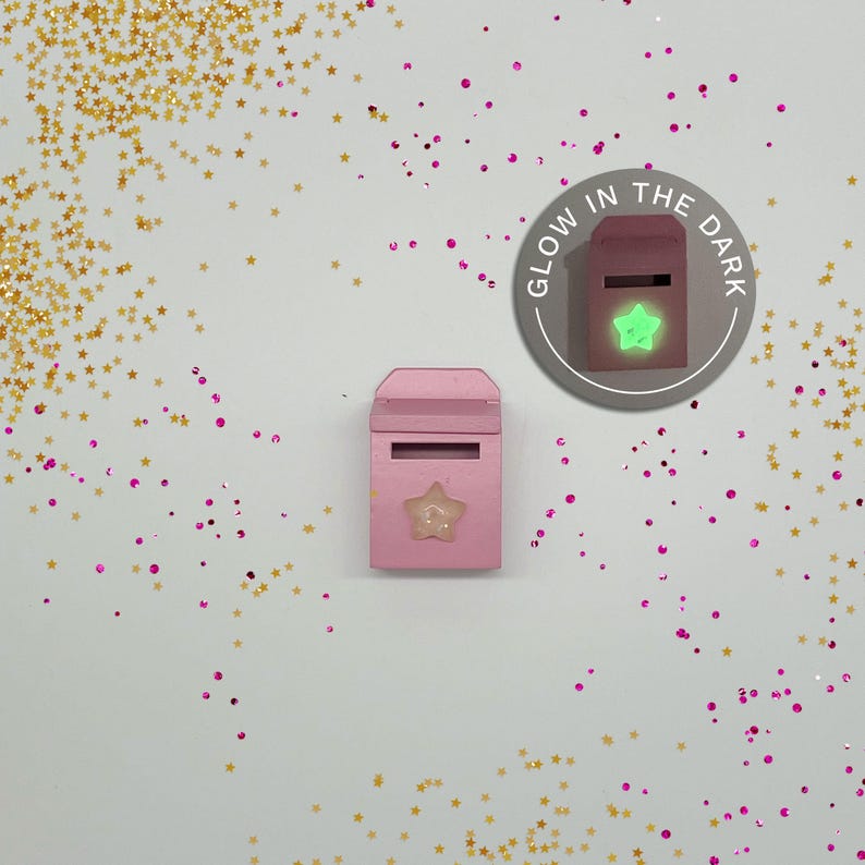 Peut inclure: Bo&icirc;te aux lettres en bois rose avec une &eacute;toile qui brille dans le noir sur le devant. La bo&icirc;te aux lettres est entour&eacute;e de paillettes dor&eacute;es et roses.