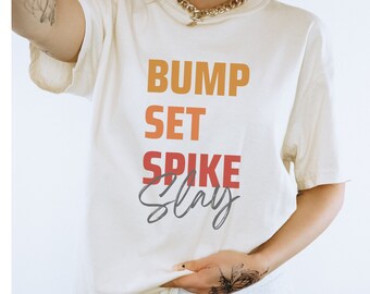 May include: White t-shirt with the text "BUMP SET SPIKE SLAY" in orange, red, and grey lettering.