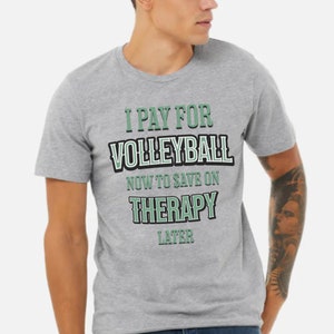 Puede incluir: Una camiseta gris con el texto "I pay for volleyball now to save on therapy later" en letras negras y verdes.