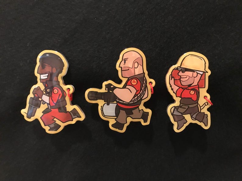 May include: Three cartoon character pins. Each pin depicts a different character in a running pose, with a red and brown colour scheme. The pins have a yellow border and a small red string attached.