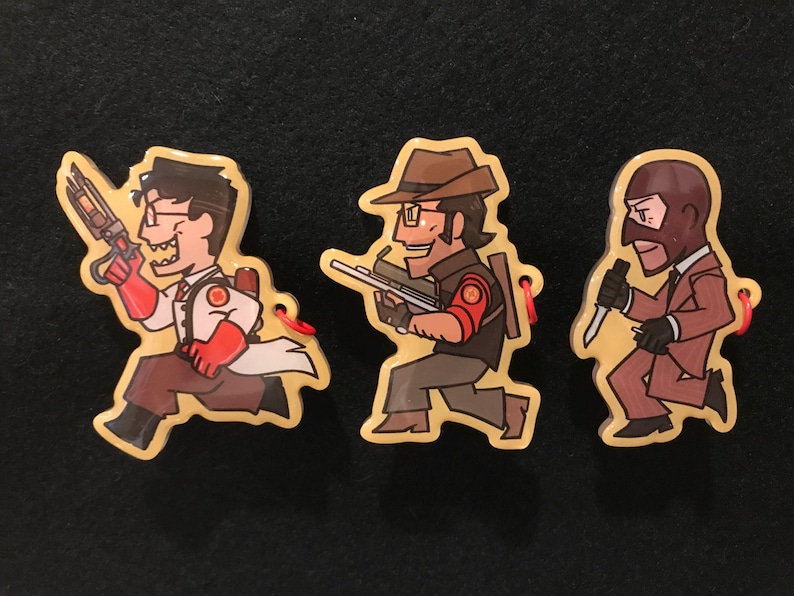 May include: Three cartoon character keyrings. The first is a doctor in a white coat and red gloves holding a weapon. The second is a man in a brown hat holding a rifle. The third is a man in a suit holding a knife.