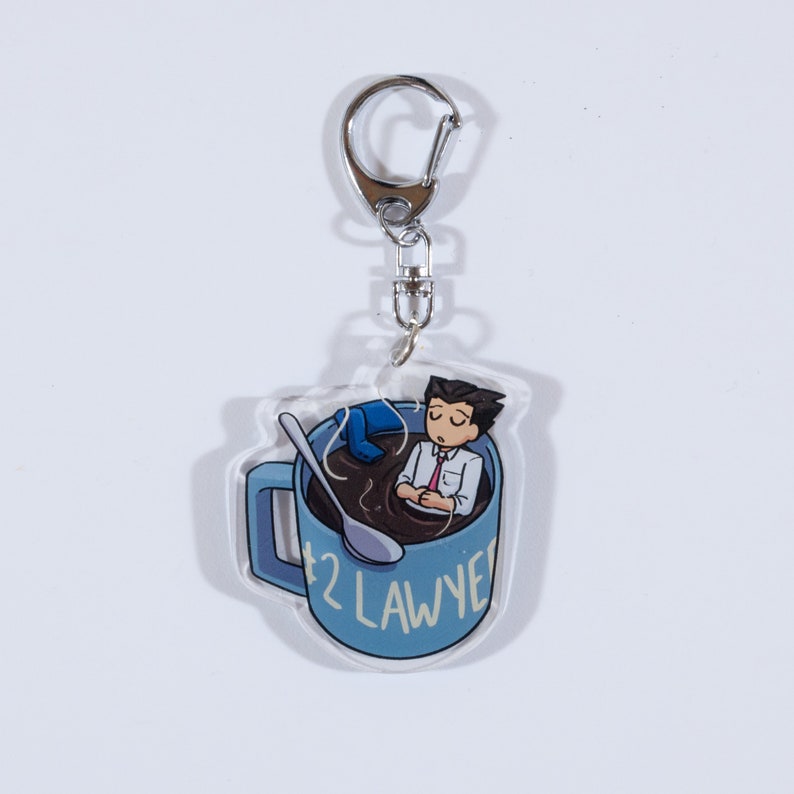 May include: A blue coffee mug with a cartoon character inside. The mug has a spoon and the text '#2 LAWYER' on the side. The mug is attached to a silver keychain.