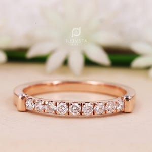 May include: A delicate rose gold band with a row of small round diamonds set in a pave setting. The band is simple and elegant, perfect for a wedding or anniversary.