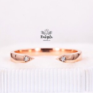 May include: Rose gold ring with a minimalist design. The ring features a small, clear gemstone set in a triangular bezel on each end. The ring is set against a white background. The brand name "Rubysta Jewels" is visible.