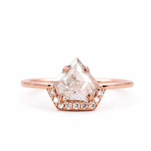 Peut inclure: Une bague en or rose ornée d'un grand diamant poivre et sel translucide en forme de bouclier, maintenu par quatre griffes. La base du sertissage est agrémentée d'une rangée de dix petits diamants blancs ronds taille brillant en or rose.