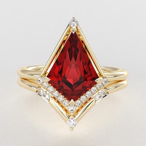 May include: A gold ring set featuring a large, kite-shaped red gemstone as the centerpiece. The setting is accented with small, round, clear stones lining the lower edges of the kite shape and a single stone at the top point, all set in polished gold.