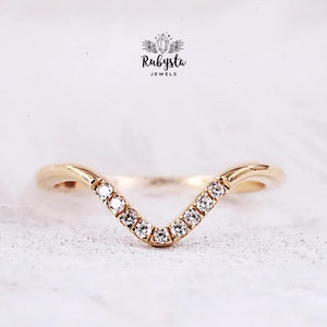 Peut inclure: Une bague en forme de V en or avec une rangée de petites pierres claires taillées en rond serties le long de la courbe centrale. Au-dessus de la bague, le texte Rubysta JEWELS est affiché avec un petit graphique de cristal entouré de feuilles.
