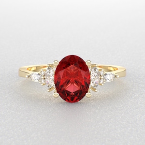 May include: A gold ring with a large oval red gemstone surrounded by smaller clear gemstones.