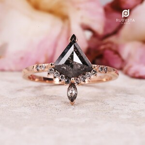Peut inclure: Une bague en or rose ornée d'un grand diamant poivre et sel en forme de cerf-volant, entouré d'un halo de petits diamants blancs ronds et d'une goutte de diamant poivre et sel taille marquise, avec des diamants supplémentaires sur l'anneau.