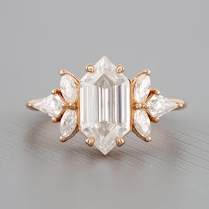 May include: A rose gold engagement ring with a large, octagon-shaped center diamond and smaller diamonds set in a floral design.