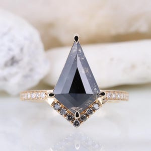 May include: A gold engagement ring with a black diamond in a kite shape. The diamond is surrounded by smaller diamonds in a halo setting. The band is set with smaller diamonds.