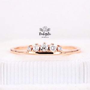 May include: A rose gold ring featuring five round, clear gemstones. The ring has a delicate band and the gemstones are set in a row across the top. The brand name "Rubysta Jewels" is visible in the background.