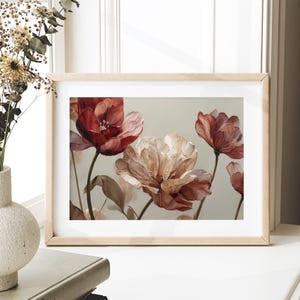 May include: A framed floral art print featuring a close-up of large, stylized flowers in shades of red, pink, and cream. The artwork is set against a soft, neutral background, and the frame is a light wood color.