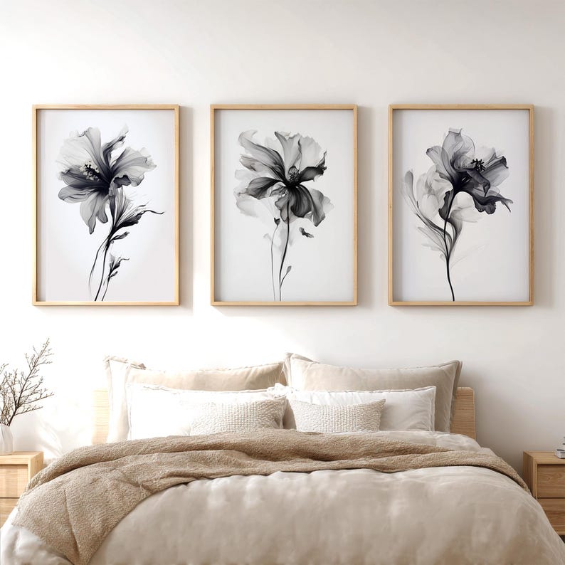 May include: Three framed floral art prints. Each print features a black and white botanical illustration of a flower. The prints are in light wood frames and are displayed above a bed with neutral-toned bedding.