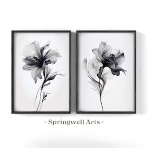 May include: Two framed floral art prints. Each print features a grayscale image of a flower with delicate petals and stems against a white background. The frames are black. The text "~ Springwell Arts ~" is at the bottom.