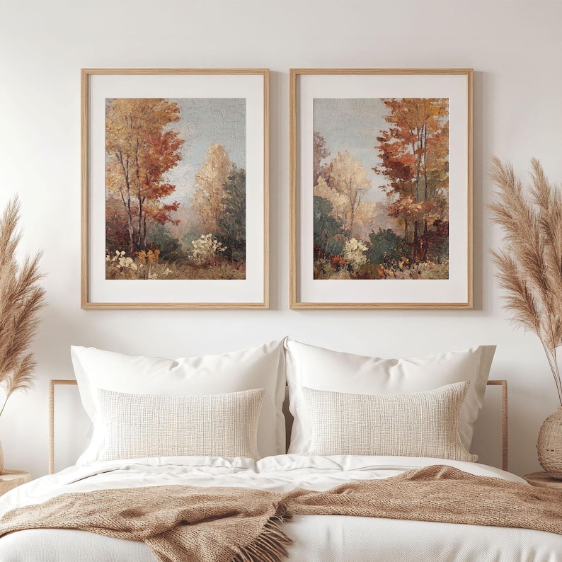 May include: Two framed landscape art prints. Each print features a forest scene with trees in shades of red, orange, and green. The artwork is displayed above a bed with white bedding and decorative pillows.