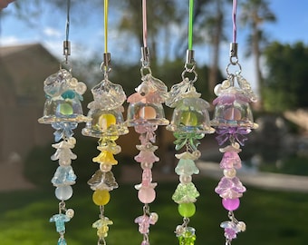 May include: Five colorful glass bell charms with beaded accents. Each charm features a clear glass bell with a different colored iridescent bead inside. The bells are attached to a string with a variety of beads and charms, including flowers, stars, and pearls.