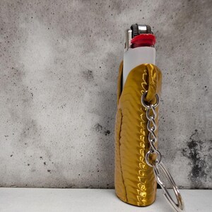 Pu&ograve; includere: Un astuccio per accendino color oro con una catena e un portachiavi. L'astuccio ha una superficie testurizzata ed &egrave; in pelle.