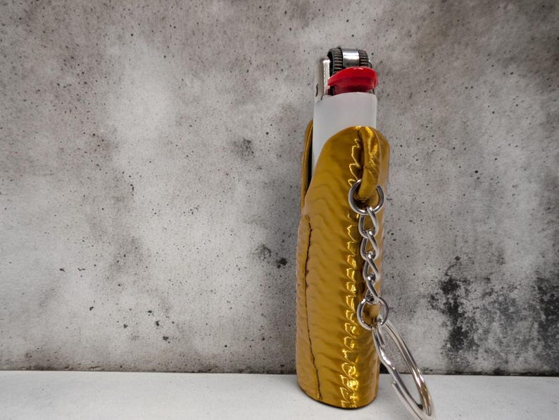 Pu&ograve; includere: Un astuccio per accendino color oro con una catena e un portachiavi. L'astuccio ha una superficie testurizzata ed &egrave; in pelle.