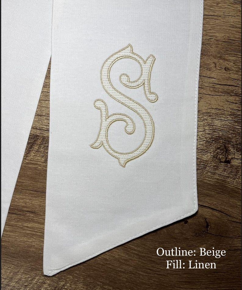 May include: White fabric with a beige embroidered letter "S". The embroidery has a decorative, ornate design. The text "Outline: Beige Fill: Linen" is visible in the lower right corner. The fabric is on a wooden surface.
