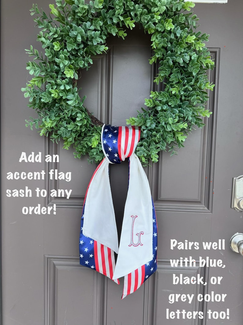 May include: A green wreath hangs on a brown door, adorned with a patriotic flag sash. The sash features a blue star pattern, red and white stripes, and a monogram. Text on the image reads: "Add an accent flag sash to any order!" and "Pairs well with blue, black, or grey color letters too!"