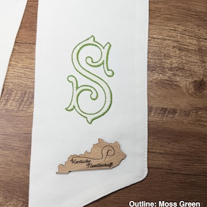 May include: White fabric sash with a green embroidered letter "S" and a wooden Kentucky-shaped emblem. The emblem has the text "Kentucky Needlecraft". The outline of the letter is moss green, and the fill is linen.