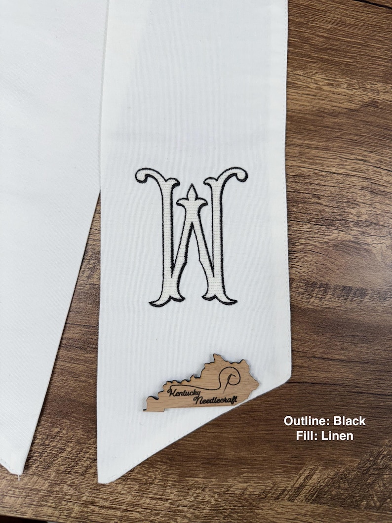 May include: White graduation stole with a black embroidered letter "W" and a wooden Kentucky-shaped embellishment. The text "Kentucky Needlecraft" is visible on the wooden embellishment. The text "Outline: Black Fill: Linen" is also visible.