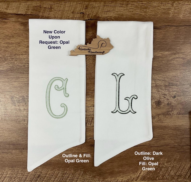 May include: Two white fabric items with embroidered letters, "C" and "L", in opal green and dark olive. The text "New Color Upon Request: Opal Green" is visible. A wooden Kentucky Needlecraft logo is also present.