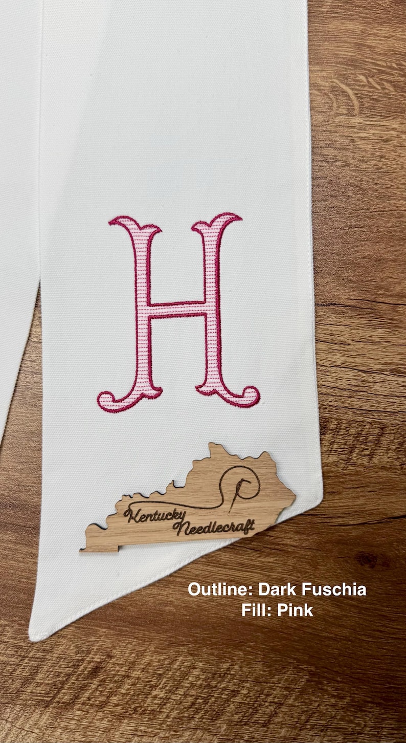 May include: White fabric with a large, embroidered pink letter "H". A wooden cutout of Kentucky with "Kentucky Needlecraft" is attached. Text at the bottom reads "Outline: Dark Fuschia Fill: Pink".