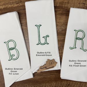 May include: Three white linen towels with embroidered letters B, L, and R in emerald green. The towels have different fill colors: linen, emerald green, and fresh green. The towels are displayed on a wooden surface.