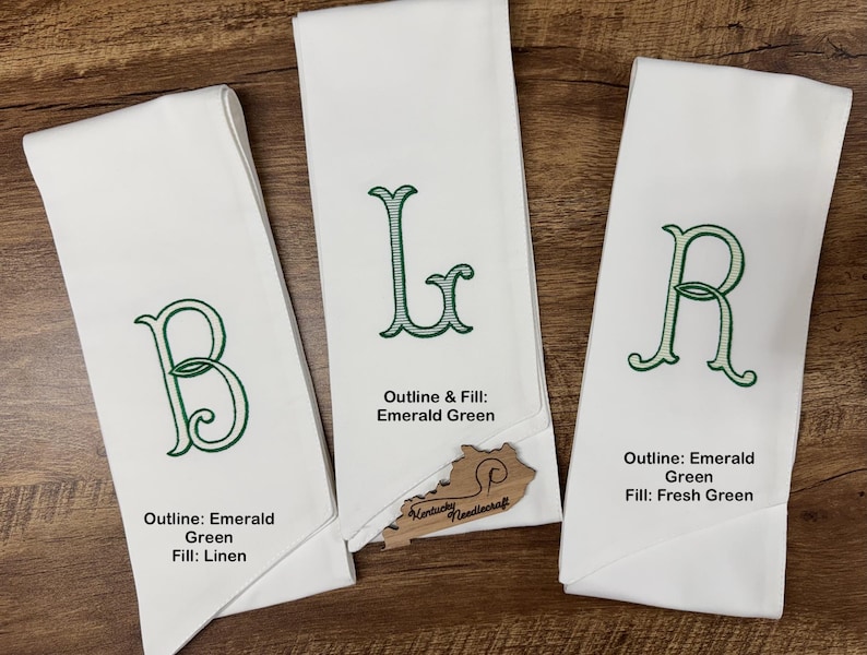 May include: Three white linen towels with embroidered letters B, L, and R in emerald green. The towels have different fill colors: linen, emerald green, and fresh green. The towels are displayed on a wooden surface.