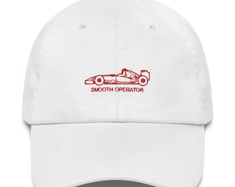 May include: A white baseball cap featuring an embroidered red graphic of a Formula One race car centered on the front panel. Below the race car, the text SMOOTH OPERATOR is embroidered in red capital letters in a simple sans-serif font.