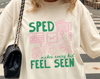 Könnte beinhalten: Ein elfenbeinfarbenes Kurzarm-T-Shirt mit grünem Text, der SPED makes every kid FEEL SEEN lautet. Das Design enthält rosa Strichzeichnungen eines Kalenders, einer mit yet beschrifteten Box, eines Regenbogens, einer Checkliste und Strichmännchen.