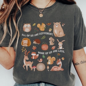 May include: Dark grey t-shirt with a woodland animal illustration, including a bear, owl, and squirrel, and the text "ALL OF US ARE DIFFERENT, NONE OF US ARE LESS."