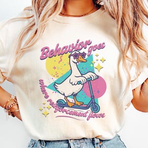 May include: Ivory t-shirt with a cartoon goose wearing sunglasses and riding a scooter. The graphic includes the text "Behavior goes where reinforcement flows" in a retro style with colourful geometric shapes and stars.