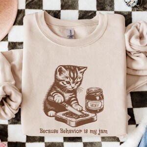 Because Behavior is my jam, with a kitten spreading jam on toast, pictured on a sand colored sweatshirt.