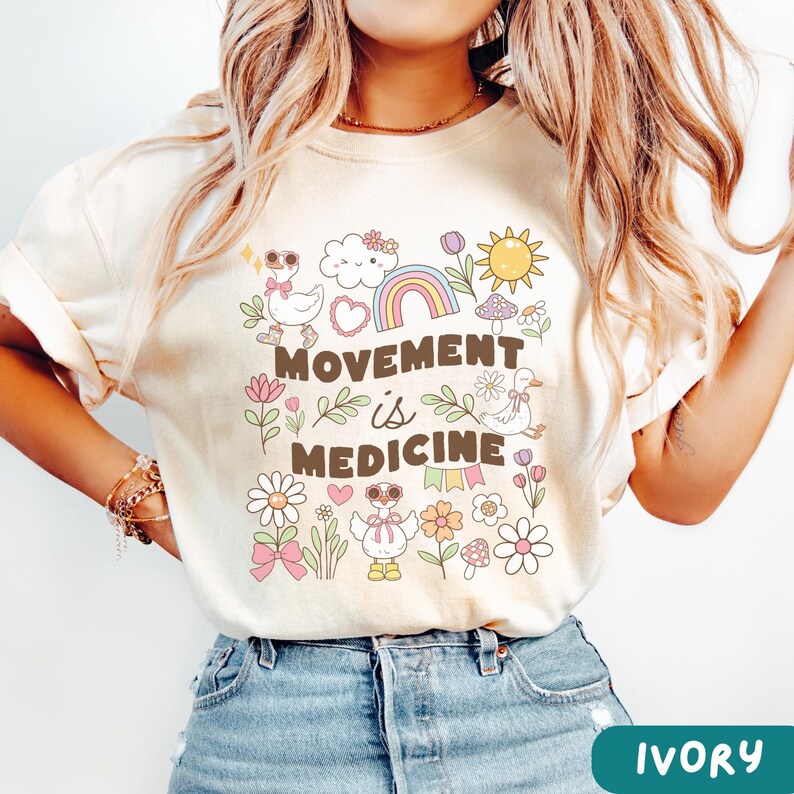 May include: Ivory t-shirt with a graphic design featuring a rainbow, clouds, flowers, mushrooms, and the text "Movement is Medicine".