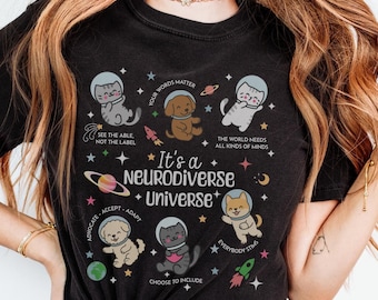 Może przedstawiać: Czarny T-shirt z grafiką przedstawiającą galaktykę z gwiazdami, planetami i rakietami. W centrum projektu znajduje się tekst "It's a Neurodiverse Universe". Grafika zawiera również zwierzęta w hełmach astronautów i tekst "Your words matter", "See the able, not the label", "The world needs all kinds of minds", "Advocate, Accept, Adapt", "Everybody stings" oraz "Choose to include".