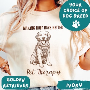 May include: Ivory-colored t-shirt featuring a Golden Retriever illustration with the text "Making Ruff Days Better" and "Pet Therapy." The design includes a dog harness with the name "Wade." The shirt also has the text "Your Choice of Dog Breed" and "Golden Retriever."