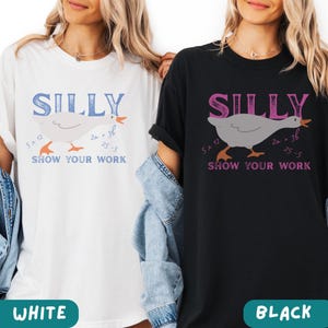 May include: White and black t-shirts with the word "SILLY" above a cartoon goose illustration. The goose has math equations around it, and the phrase "SHOW YOUR WORK" is below. The bottom of the shirts have the words "WHITE" and "BLACK".