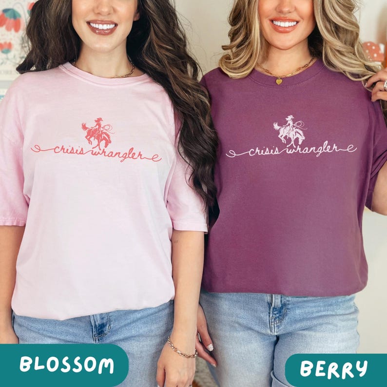 K&ouml;nnte beinhalten: Zwei Frauen tragen T-Shirts mit dem Text "crisis wrangler" und einer Grafik einer Cowgirl, die ein Pferd reitet. Die Frau links tr&auml;gt ein rosa T-Shirt und die Frau rechts tr&auml;gt ein lila T-Shirt.