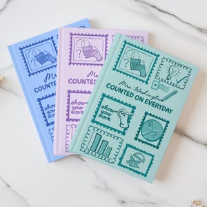 May include: Three notebooks in pastel colors: blue, lavender, and mint green. Each notebook features a stamp-like design with illustrations of a calculator, lightbulb, and other work-related graphics. The text "Mrs. Washington Counted on Everyday" is visible on the green notebook.
