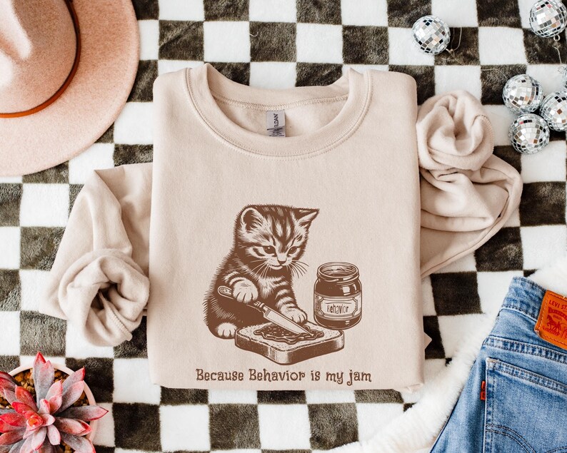 Because Behavior is my jam, with a kitten spreading jam on toast, pictured on a sand colored sweatshirt.